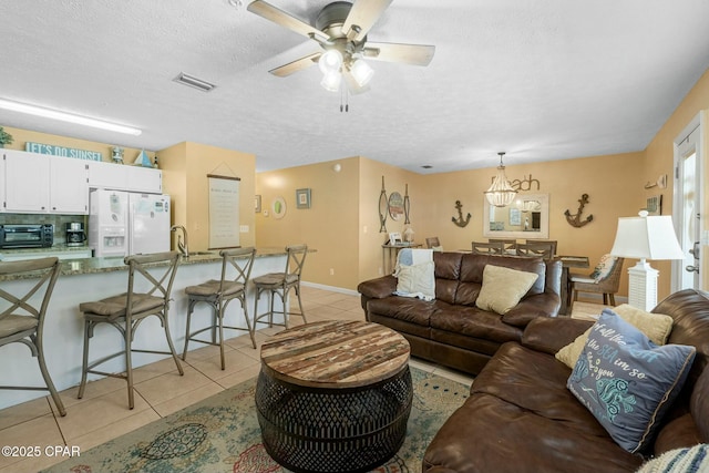 living area with light tile patterned floors, a textured ceiling, a toaster, a ceiling fan, and visible vents