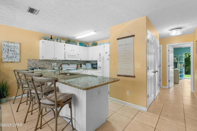 kitchen with light tile patterned flooring, a peninsula, white appliances, a sink, and visible vents