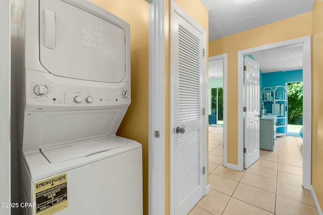 washroom with a textured ceiling, laundry area, light tile patterned floors, and stacked washer and clothes dryer