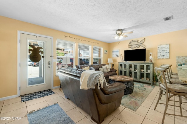 living area with light tile patterned floors, visible vents, ceiling fan, a textured ceiling, and baseboards