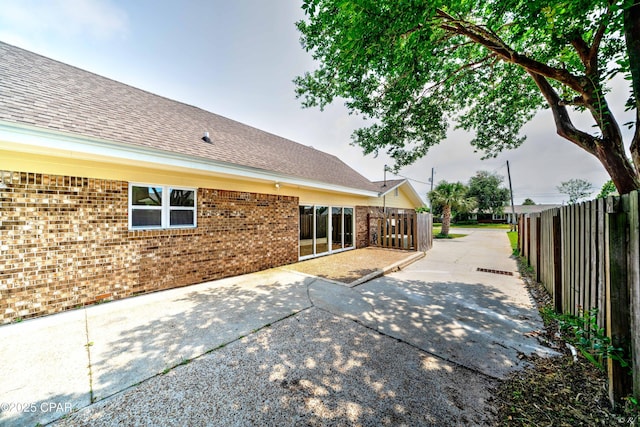 rear view of house with a shingled roof, brick siding, fence, and a patio