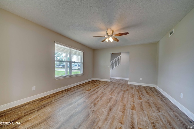 empty room with baseboards, stairway, visible vents, and light wood-style floors