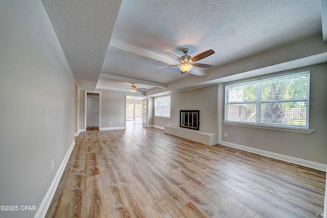 unfurnished living room with baseboards, a ceiling fan, a textured ceiling, light wood-type flooring, and a fireplace