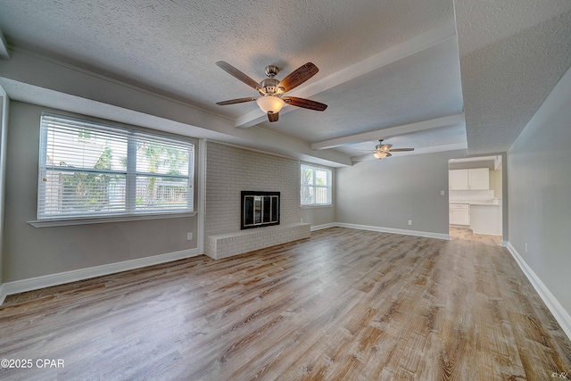 unfurnished living room featuring a textured ceiling, a fireplace, baseboards, light wood-type flooring, and beamed ceiling