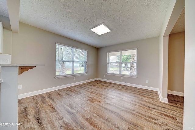 unfurnished living room with light wood-style flooring, baseboards, and a textured ceiling