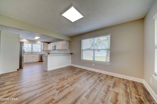 interior space with stainless steel appliances, white cabinetry, light wood-style flooring, and a peninsula