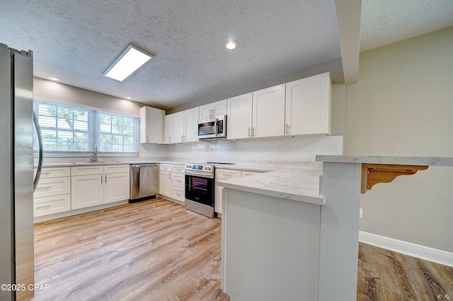 kitchen featuring light wood finished floors, appliances with stainless steel finishes, white cabinetry, a sink, and a peninsula