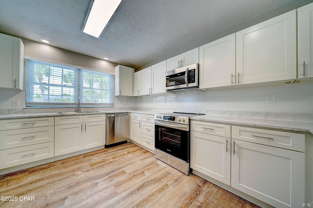 kitchen with decorative backsplash, appliances with stainless steel finishes, light wood-style floors, white cabinets, and a sink