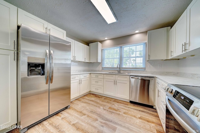 kitchen with light wood-style flooring, stainless steel appliances, a sink, white cabinets, and light stone countertops