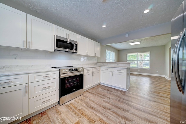 kitchen with baseboards, appliances with stainless steel finishes, a peninsula, light wood-type flooring, and white cabinetry