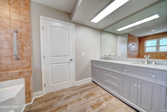 full bath featuring double vanity, tiled shower, a sink, and wood finished floors