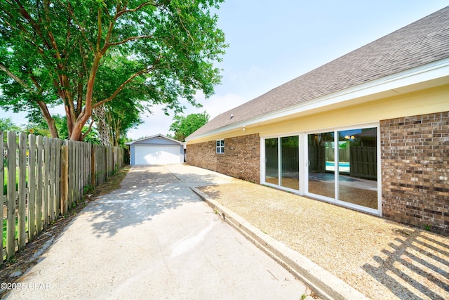 view of side of home with driveway, fence, an outdoor structure, and brick siding