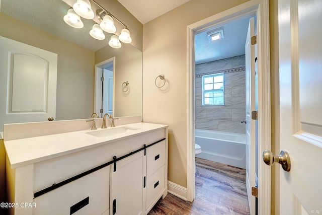 bathroom with toilet, a textured ceiling, vanity, wood finished floors, and baseboards