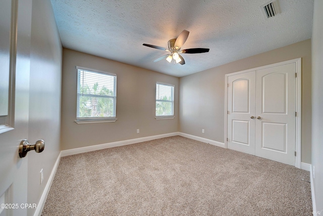 unfurnished bedroom with a textured ceiling, visible vents, baseboards, a closet, and carpet