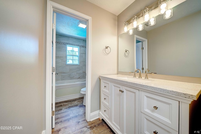 full bath featuring a textured ceiling, toilet, wood finished floors, vanity, and washtub / shower combination