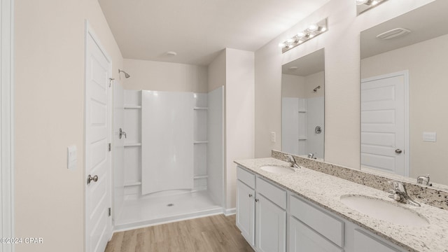 full bath with wood finished floors, a shower, double vanity, and a sink