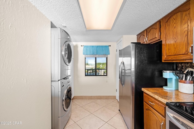 kitchen featuring light tile patterned floors, a textured ceiling, stacked washer and dryer, light countertops, and brown cabinets