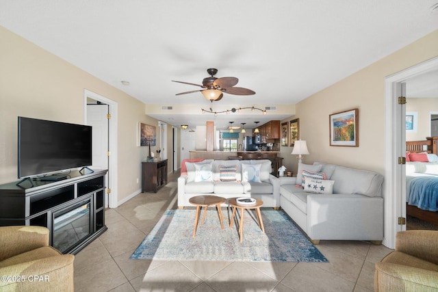 living area featuring light tile patterned floors, ceiling fan, and baseboards