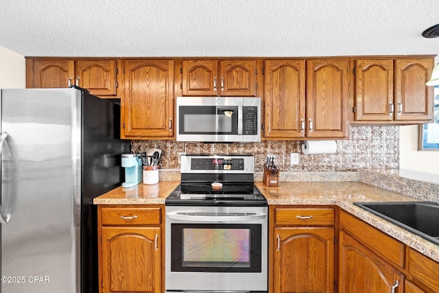 kitchen featuring stainless steel appliances, light countertops, brown cabinetry, and backsplash