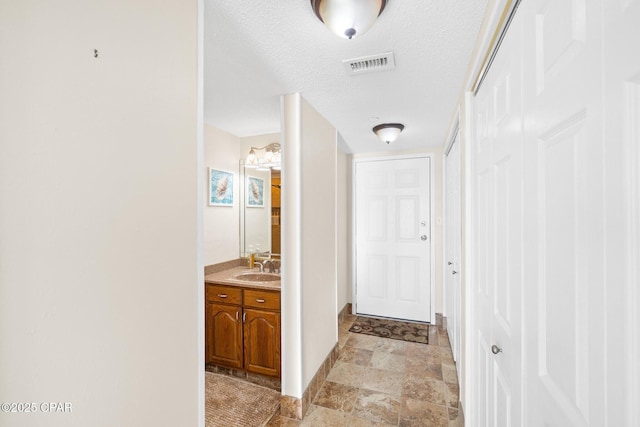 corridor with baseboards, visible vents, stone finish flooring, a textured ceiling, and a sink