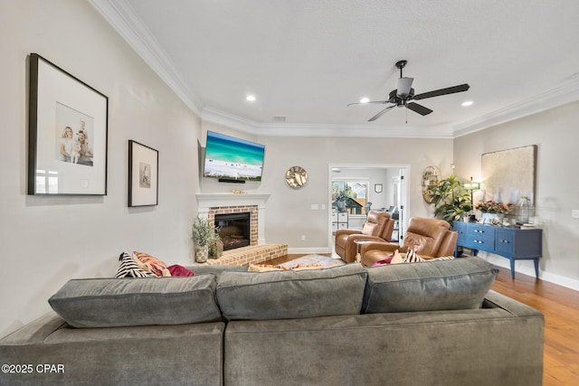 living room with hardwood / wood-style flooring, ceiling fan, crown molding, and a brick fireplace