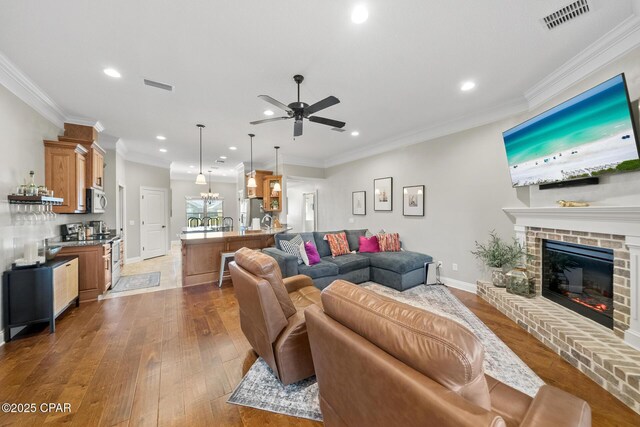 living room with a brick fireplace, ceiling fan, crown molding, and dark hardwood / wood-style floors