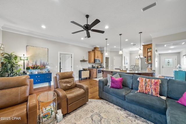 living room featuring ceiling fan with notable chandelier, light hardwood / wood-style flooring, sink, and crown molding