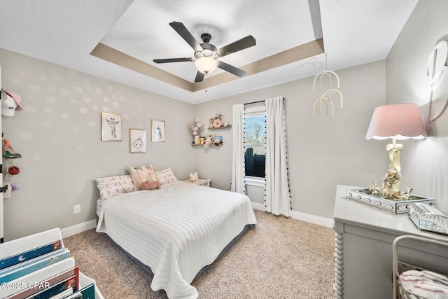 bedroom with a tray ceiling, a textured ceiling, light colored carpet, and ceiling fan