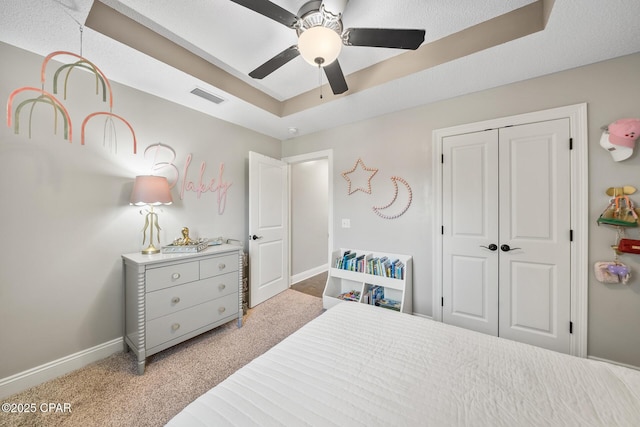 carpeted bedroom with a tray ceiling, a closet, and ceiling fan