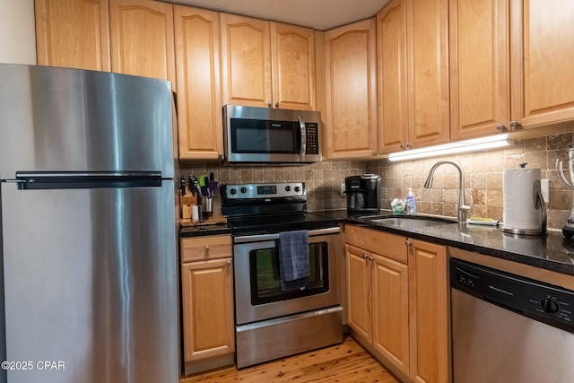 kitchen with appliances with stainless steel finishes, light wood-type flooring, a sink, and tasteful backsplash