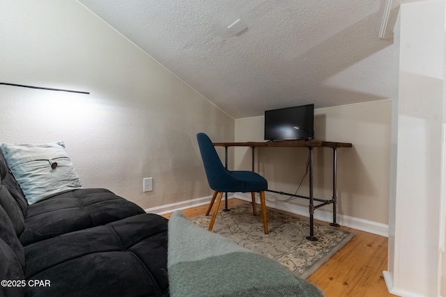 home office featuring vaulted ceiling, a textured ceiling, light wood-style flooring, and baseboards