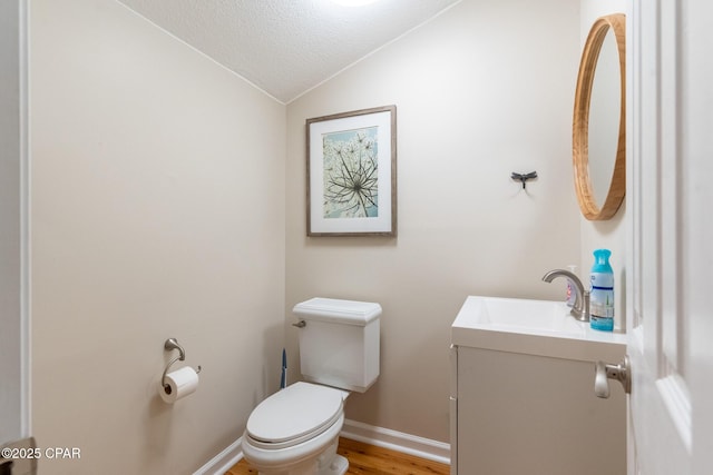 half bath featuring lofted ceiling, a textured ceiling, toilet, wood finished floors, and vanity