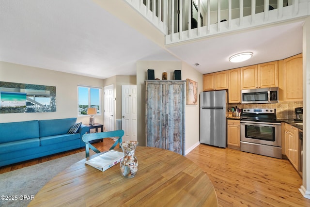 kitchen featuring light brown cabinets, stainless steel appliances, decorative backsplash, light wood finished floors, and dark countertops