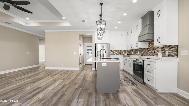 kitchen featuring a center island with sink, premium range hood, stainless steel appliances, white cabinets, and a raised ceiling