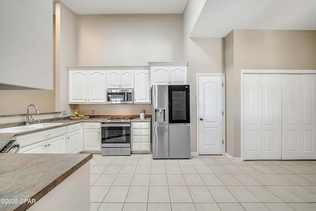 kitchen with appliances with stainless steel finishes, light tile patterned flooring, a sink, and white cabinetry