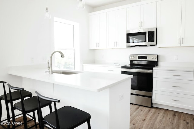 4112 Snapper St, Panama City Beach, FL 32408 - kitchen with white cabinets, appliances with stainless steel finishes, a sink, light wood-type flooring, and a kitchen breakfast bar