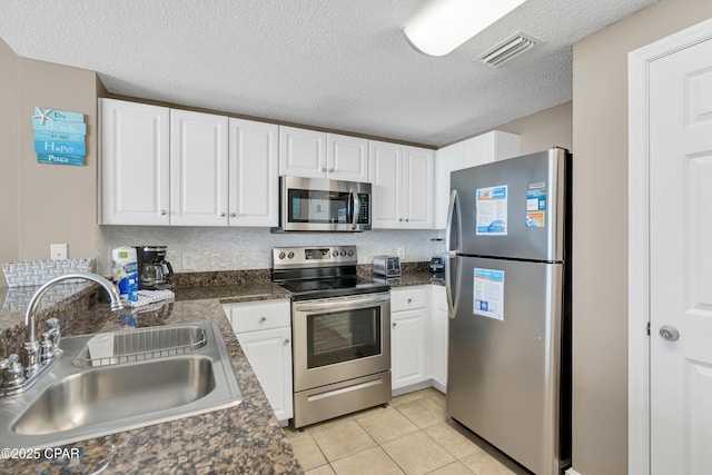 kitchen featuring light tile patterned flooring, a sink, white cabinets, appliances with stainless steel finishes, and dark countertops