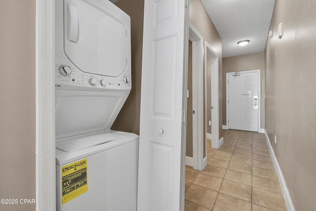 clothes washing area with baseboards, stacked washer and dryer, light tile patterned floors, laundry area, and a textured ceiling