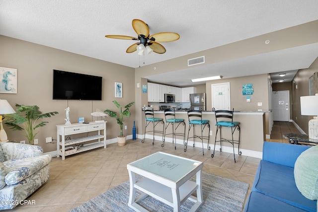 living room featuring visible vents, baseboards, ceiling fan, light tile patterned floors, and a textured ceiling