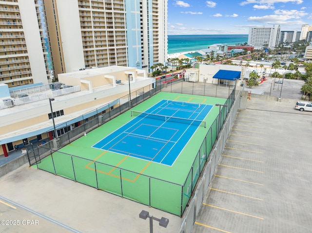 view of sport court with a water view, fence, and a city view