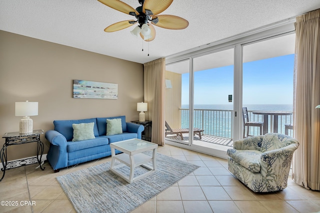 living area featuring ceiling fan, a water view, a wall of windows, light tile patterned floors, and a textured ceiling