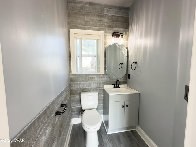 half bathroom with toilet, wood finished floors, vanity, and tile walls