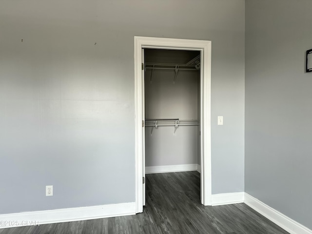 unfurnished bedroom with dark wood-style floors, a closet, a spacious closet, and baseboards