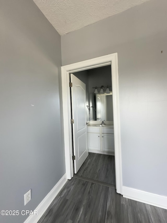 corridor with dark wood-style floors, a textured ceiling, and baseboards