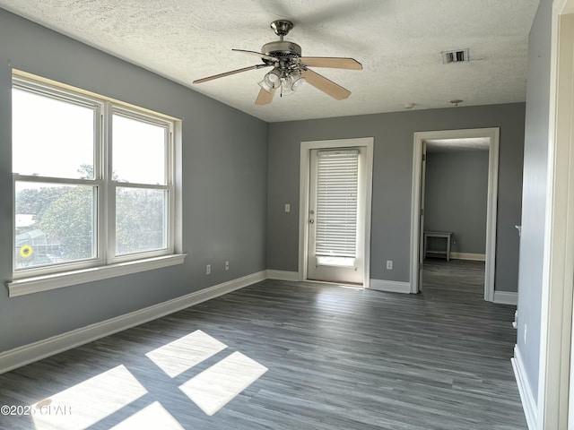 unfurnished room with a textured ceiling, dark wood-style flooring, visible vents, and baseboards