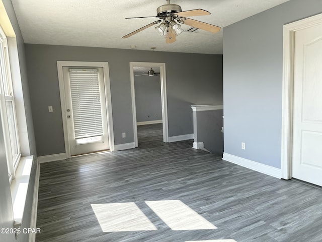 empty room with dark wood-style flooring, ceiling fan, a textured ceiling, and baseboards