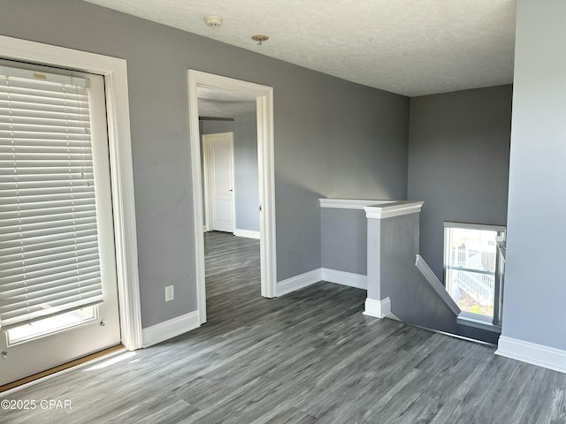 unfurnished room featuring a textured ceiling, baseboards, and wood finished floors