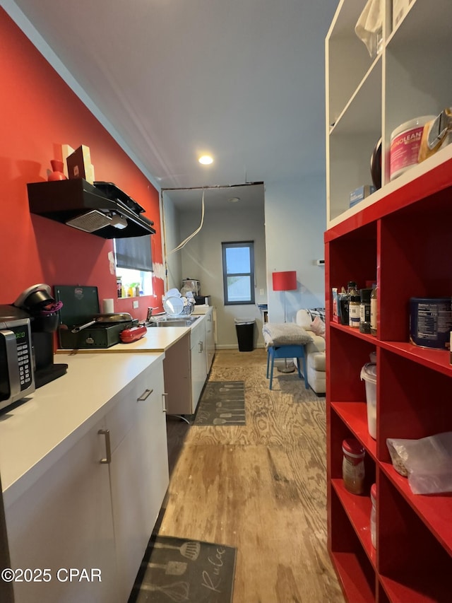 kitchen featuring washing machine and clothes dryer, light countertops, stainless steel microwave, wood finished floors, and extractor fan