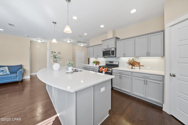 kitchen featuring a center island with sink, visible vents, hanging light fixtures, stainless steel appliances, and light countertops