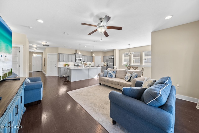 living area featuring recessed lighting, baseboards, dark wood-type flooring, and ceiling fan with notable chandelier